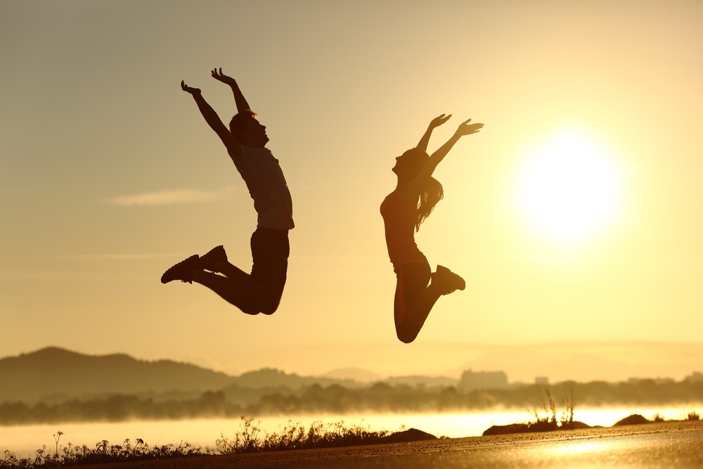 happy couple jumping , sunset in background